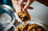 Hands carefully spreading koji starter on steamed rice in a rustic ceramic bowl.