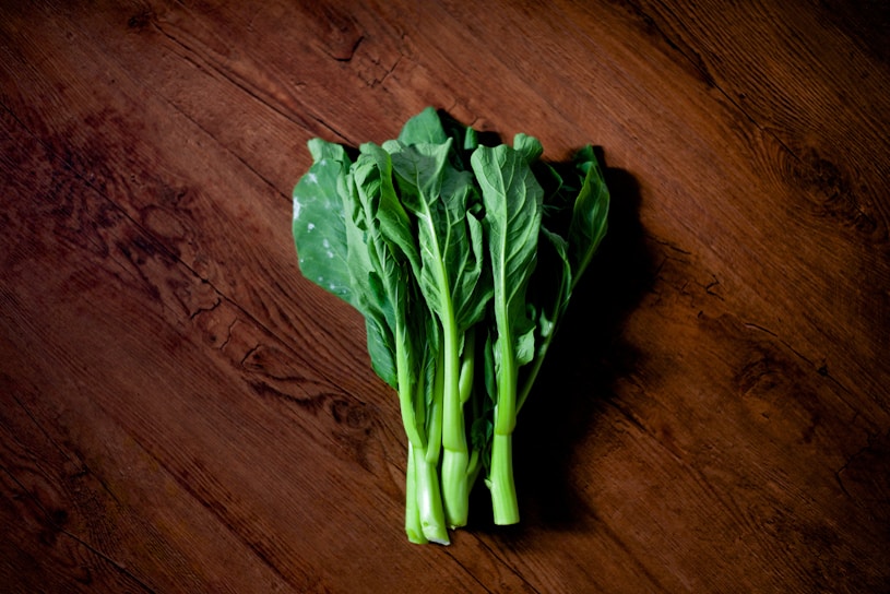 Freshly harvested green vegetables laid out on a rustic wooden table with morning sunlight.