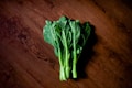 A bunch of fresh green leafy vegetables is placed on a rustic wooden surface. The leaves are vibrant and healthy, with dark green hues and crisp texture.