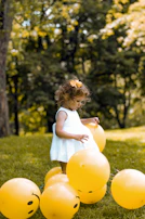 A joyful child wearing a bright yellow bow, smiling widely while surrounded by colorful balloons.