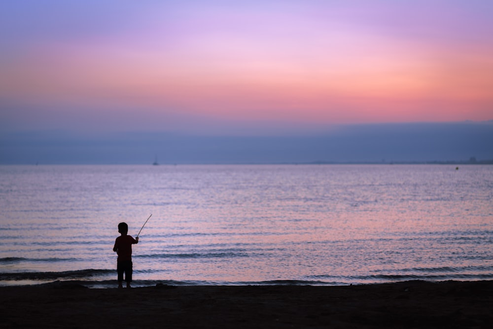 silhouette photography of toddler fishing on body of water