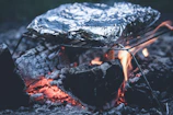 Campfire scene showing foil-wrapped beef and potatoes cooking in glowing embers.