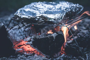 Campfire scene showing foil-wrapped beef and potatoes cooking in glowing embers.