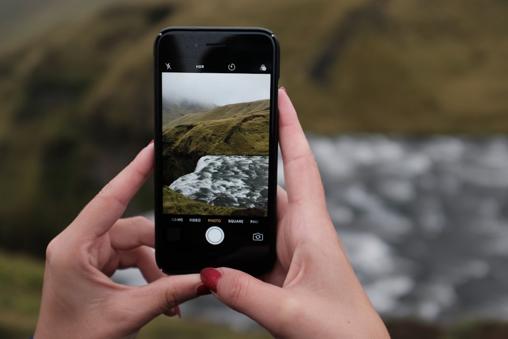 person taking photo of green hill