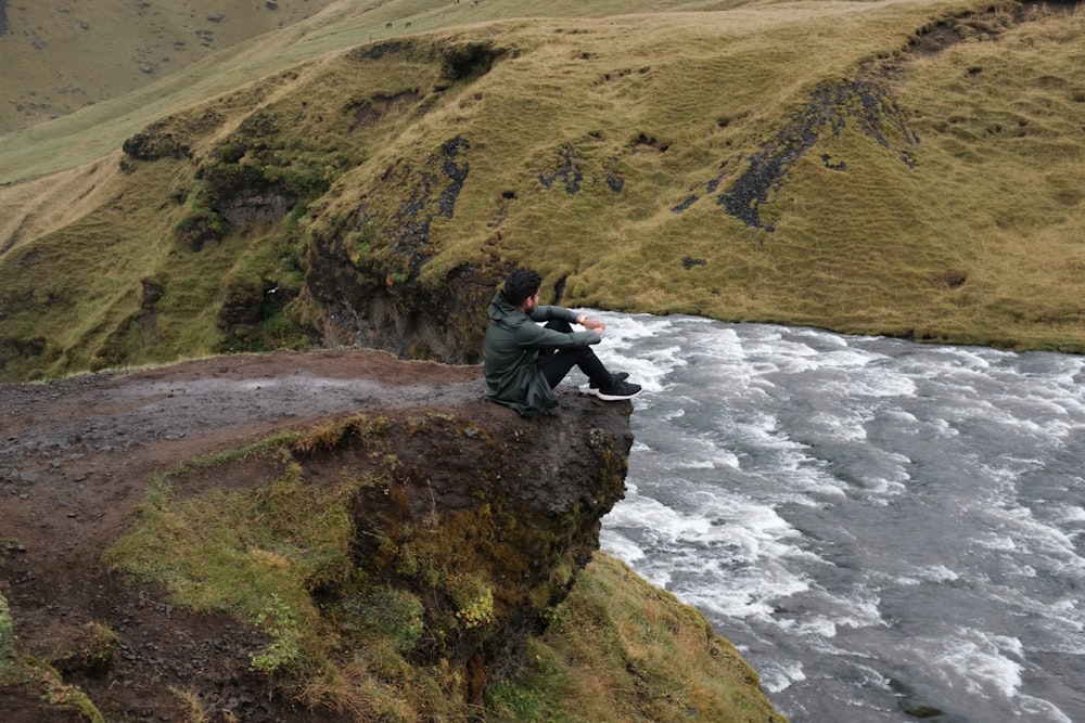 El hombre se sienta en la montaña cerca del cuerpo de agua