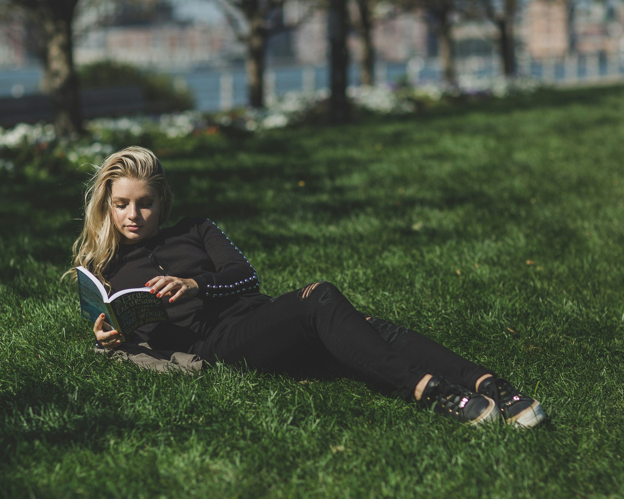 woman reading book leaning on green grass field