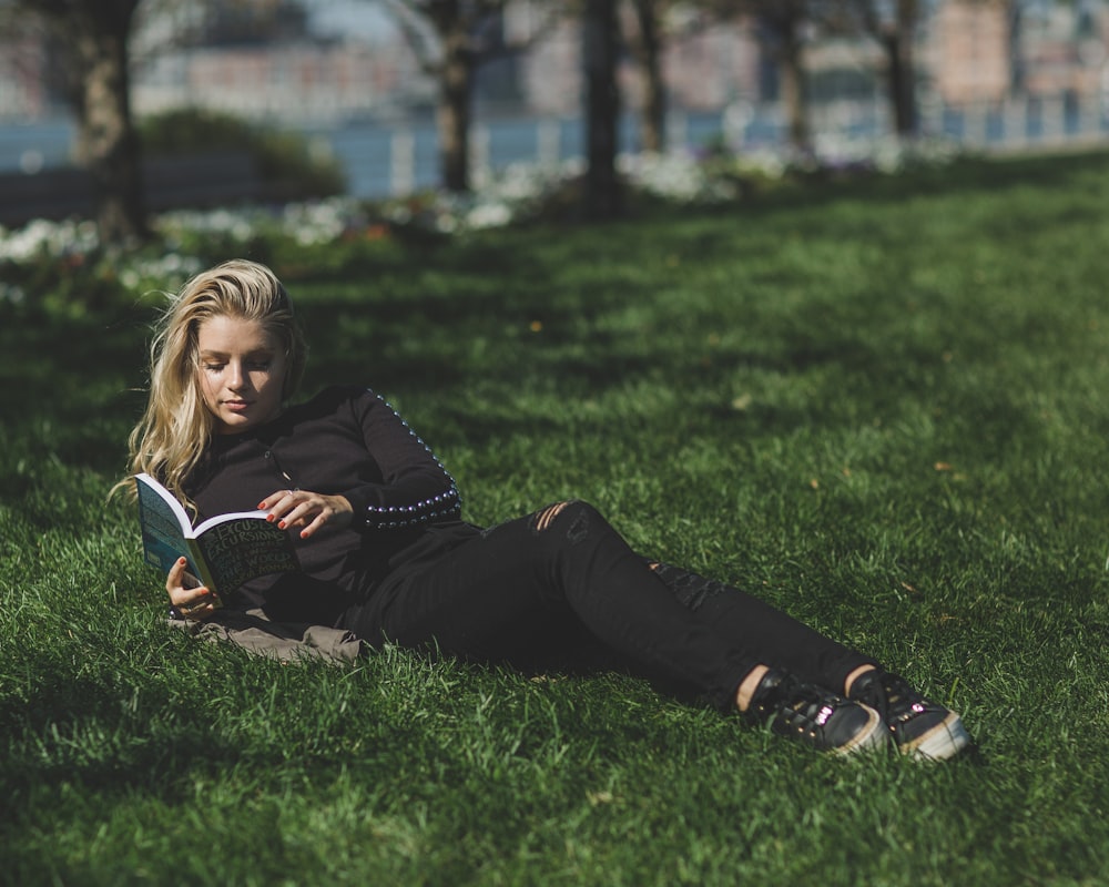 woman reading book leaning on green grass field