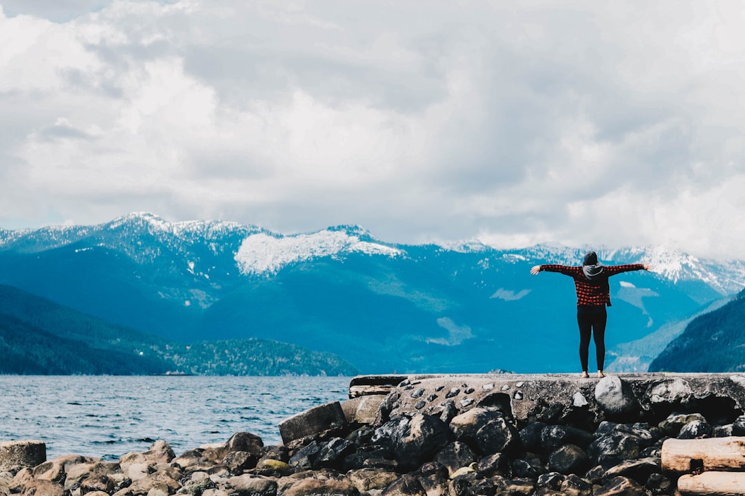 person spreading arms near water and mountain range