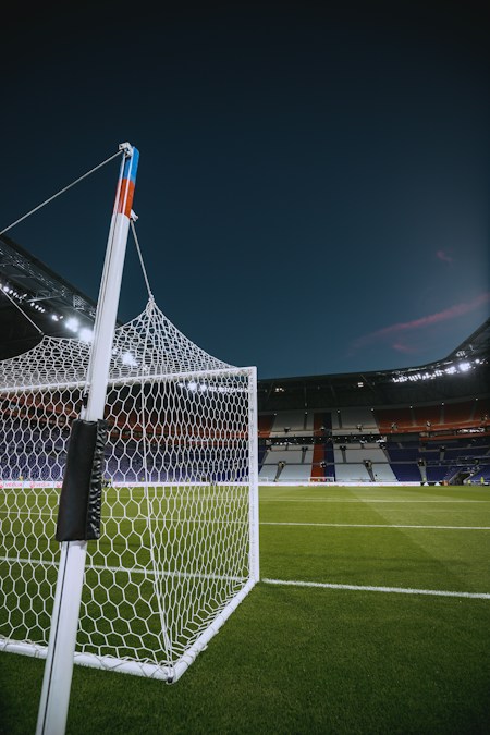 Filet d’un but de football au premier plan, dans un stade aux tribunes vides éclairé à la tombée de la nuit
