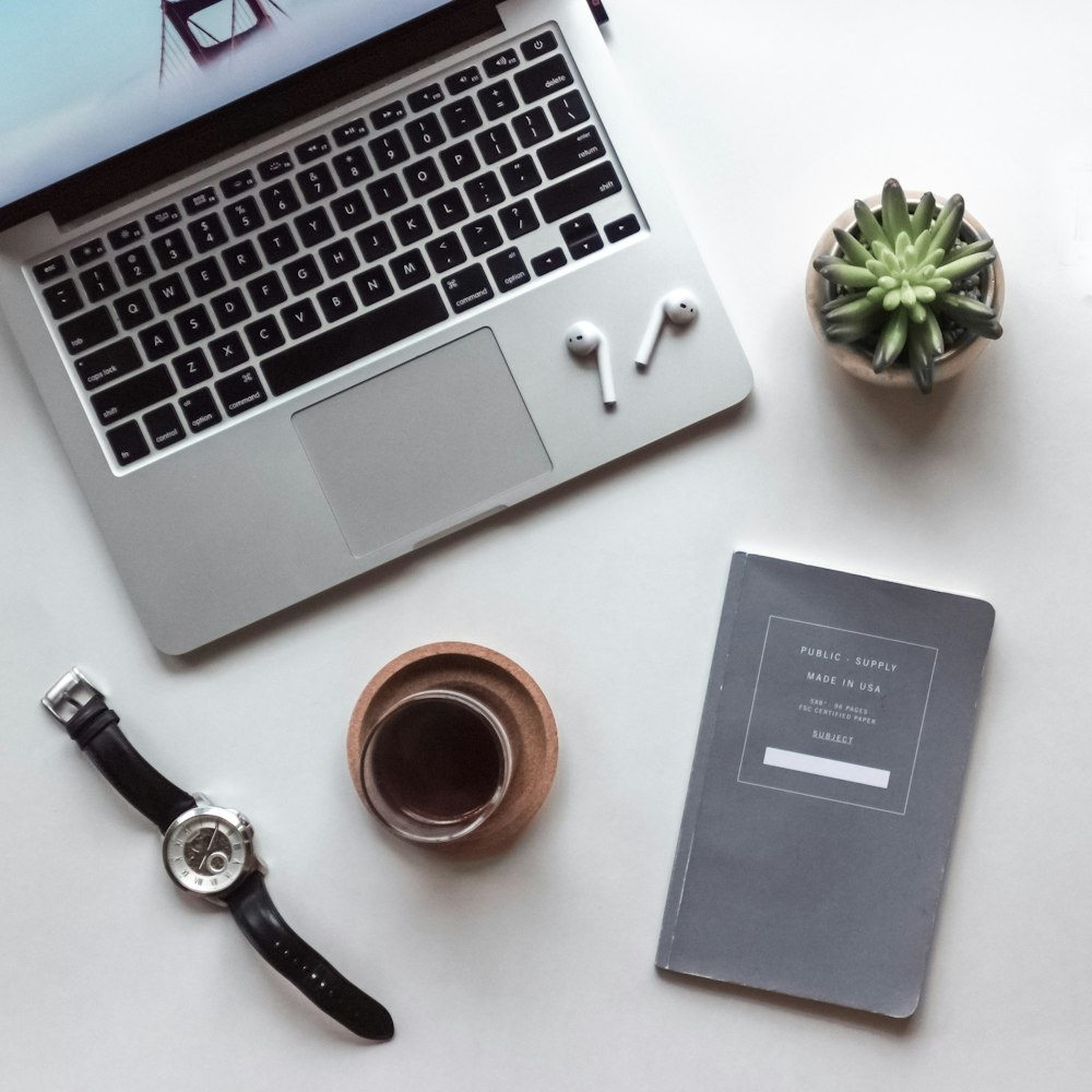 fotografia flat-lay di MacBook, tazza piena di caffè, libro e orologio da polso