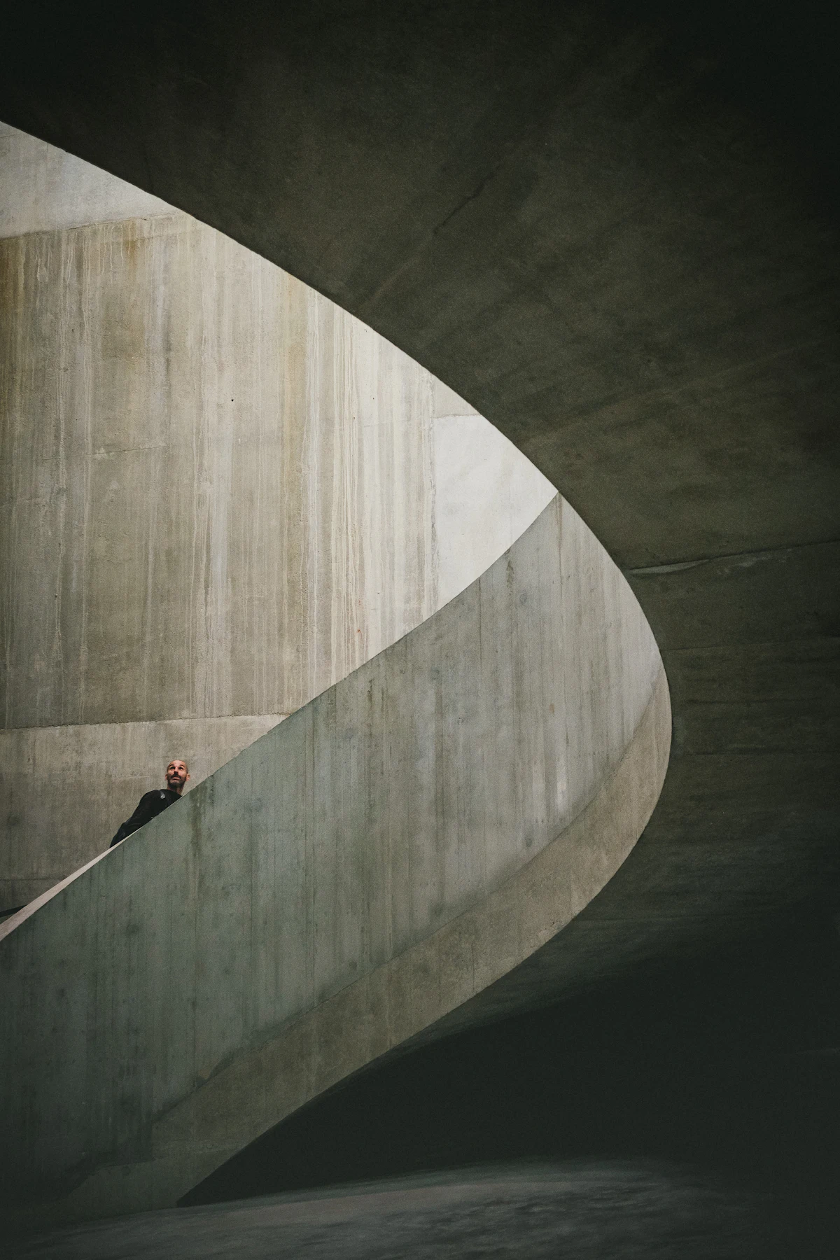 A lone figure climbing a sweeping curved concrete staircase