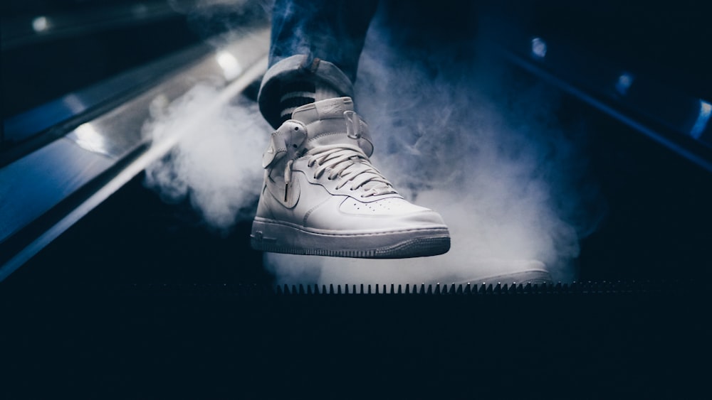 person wearing white Nike Air Force 1 mid-rise shoes while standing on escalator