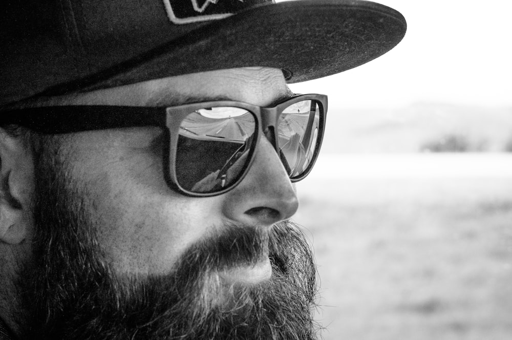 Graustufenfotografie eines Mannes mit Sonnenbrille und Hut