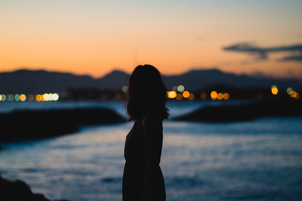 silhouette of woman standing beside body of water