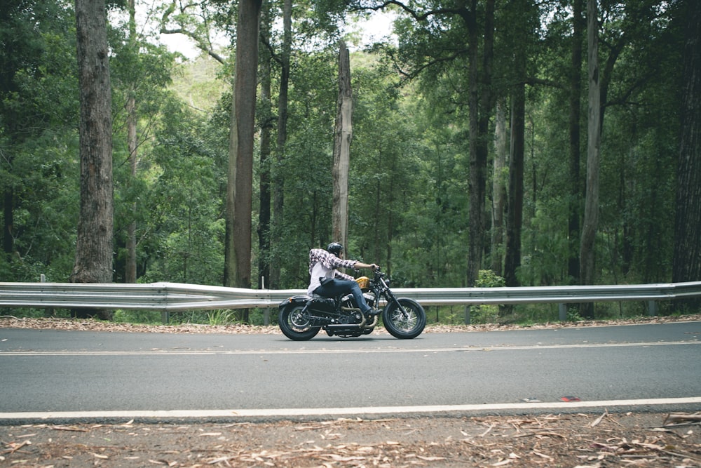 person riding motorcycle passing on road surround by trees