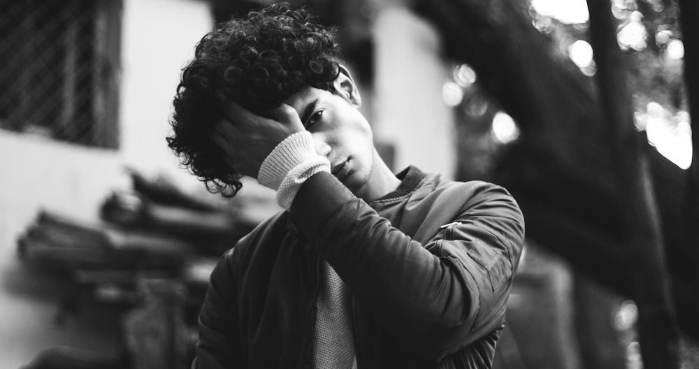 grayscale photo of man in jacket putting his palm on his forehead