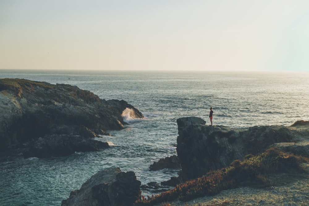 person standing on cliff near body of water