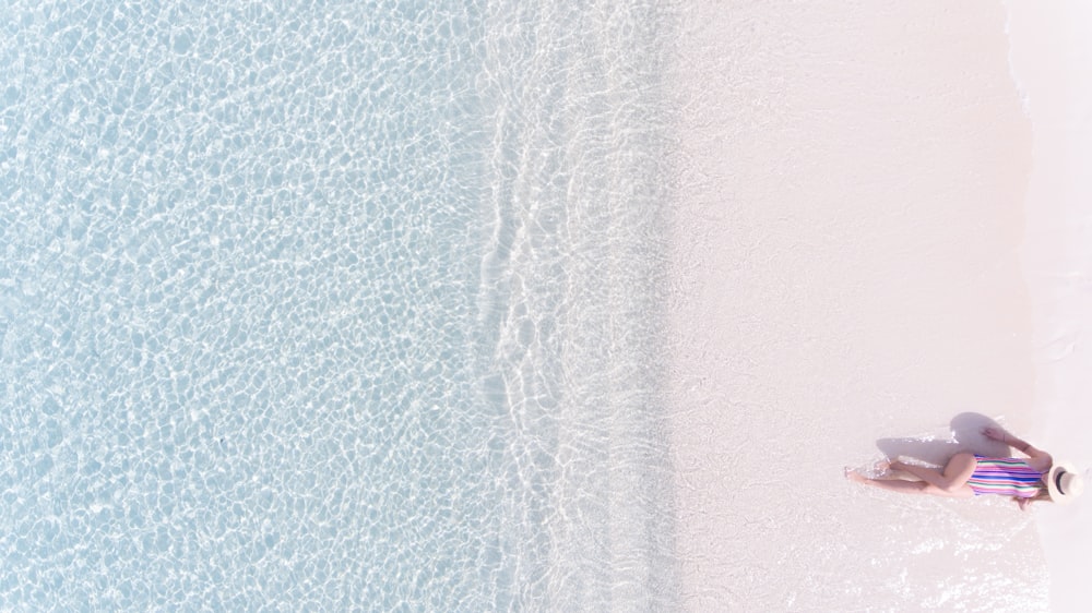 Fotografía de vista aérea de mujer tomando el sol en la orilla del mar