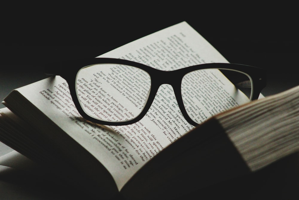 black framed eyeglasses on top of open book