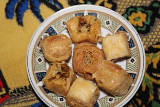 A decorative plate holds various pieces of baklava and other Middle Eastern pastries, with a detailed and colorful fabric underneath.