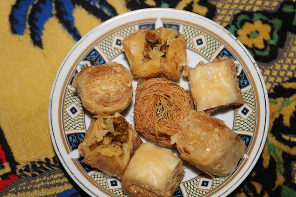 A decorative plate holds various pieces of baklava and other Middle Eastern pastries, with a detailed and colorful fabric underneath.