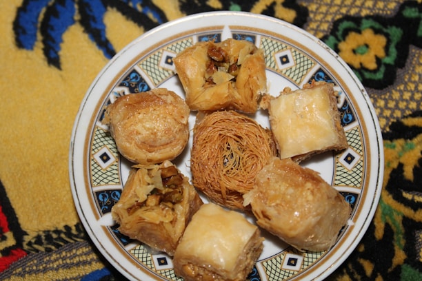 A decorative plate holds various pieces of baklava and other Middle Eastern pastries, with a detailed and colorful fabric underneath.