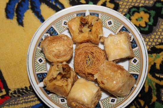 A decorative plate holds various pieces of baklava and other Middle Eastern pastries, with a detailed and colorful fabric underneath.