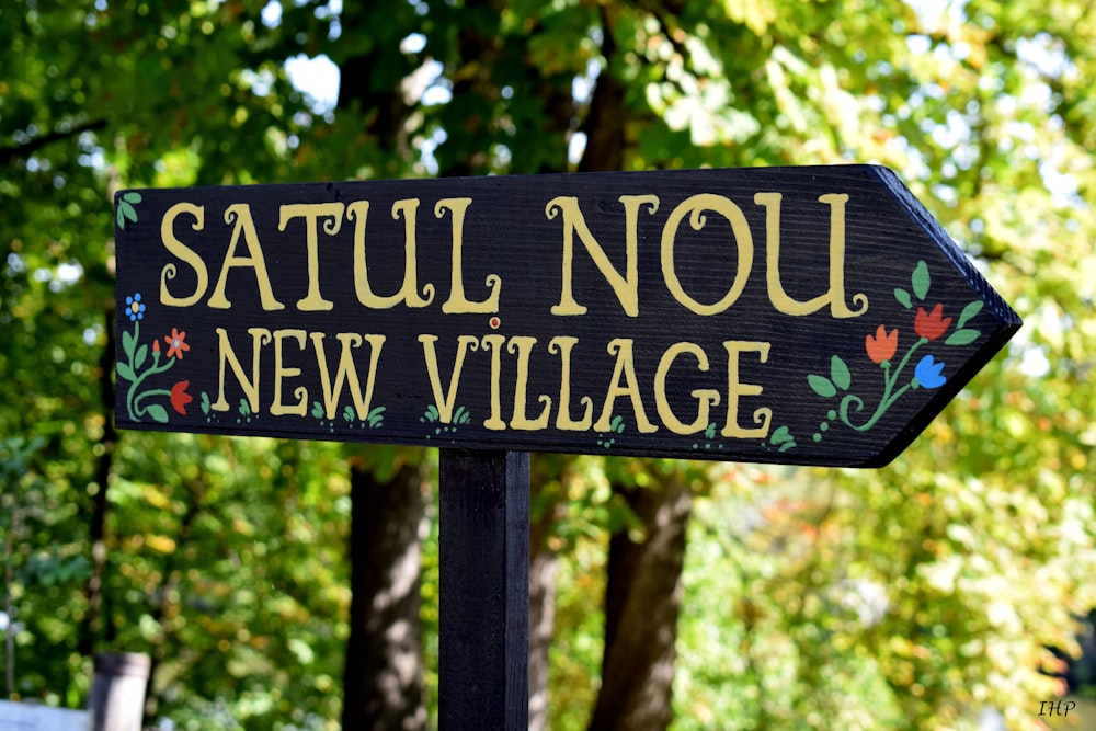 Satul Nou New Village signage under green trees