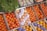 An assortment of fresh produce displayed in wooden crates includes oranges, grapefruits, and leafy greens. Some grapefruits are wrapped in white paper, while others are bare. Crisp vegetables and vibrant fruits are neatly arranged, creating a colorful display. Bags of garlic are visible in the background.