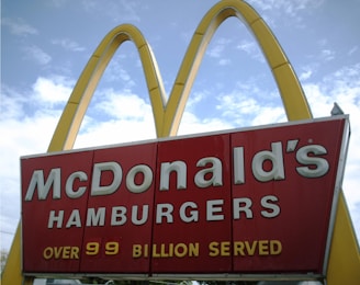 A McDonald's advertisement sign with the iconic golden arches and text declaring 'Over 99 Billion Served'. The sky is partly cloudy in the background.