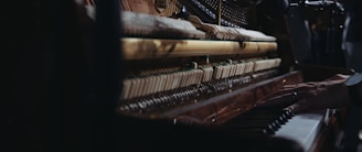 Close-up view of the inner mechanisms of an upright piano with a person's hand playing the keys, capturing the intricate details of the strings and hammers.
