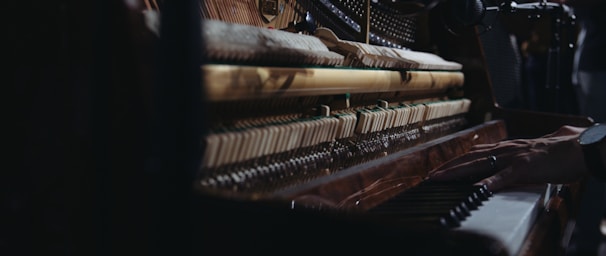 Close-up view of the inner mechanisms of an upright piano with a person's hand playing the keys, capturing the intricate details of the strings and hammers.