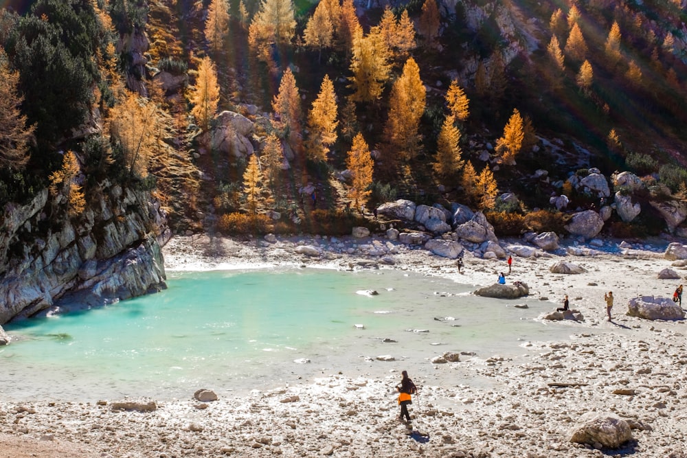 people standing beside stream with hill in distance