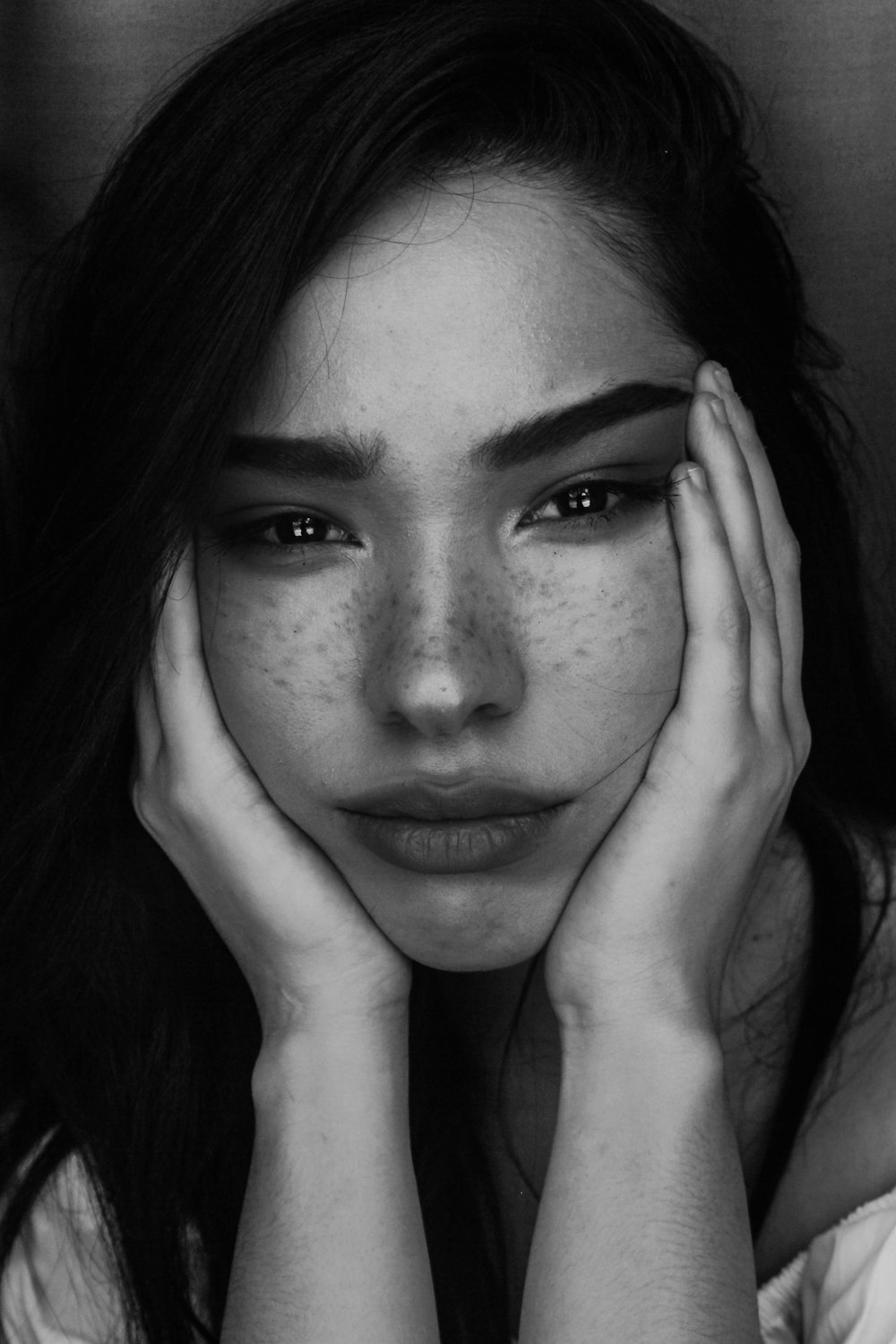 Photographie en niveaux de gris d’une femme avec deux mains sur son visage