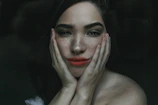 Editorial style photo of a woman gently touching her cheek, golden light highlighting skin.