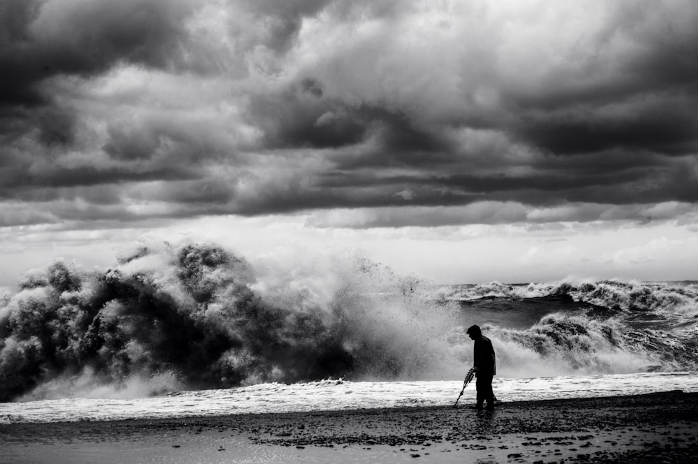 grayscale photo of man walking on seashore