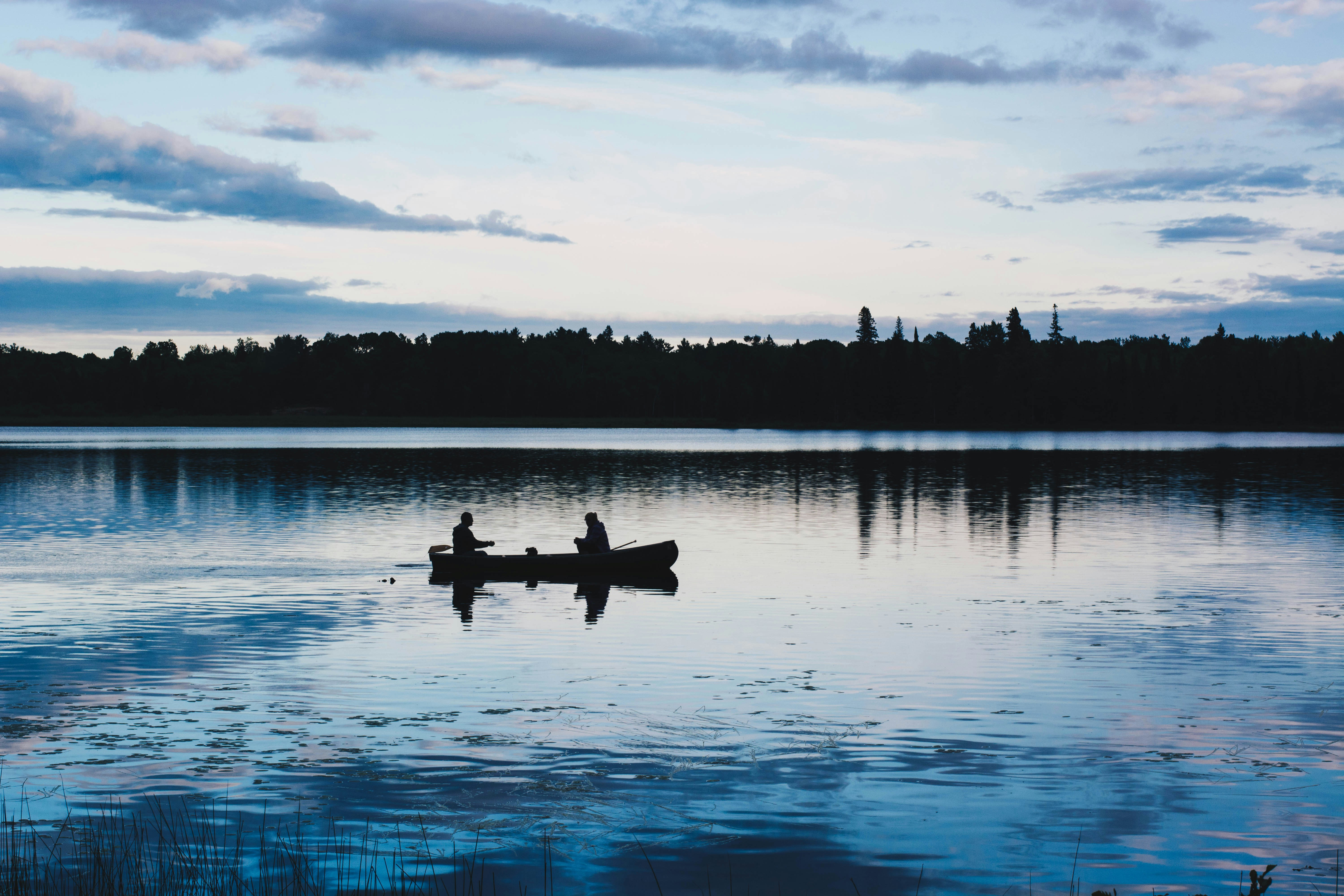 Canoe on glassy wilderness lake at dawn, dark treeline silhouette against pale sky, still water
