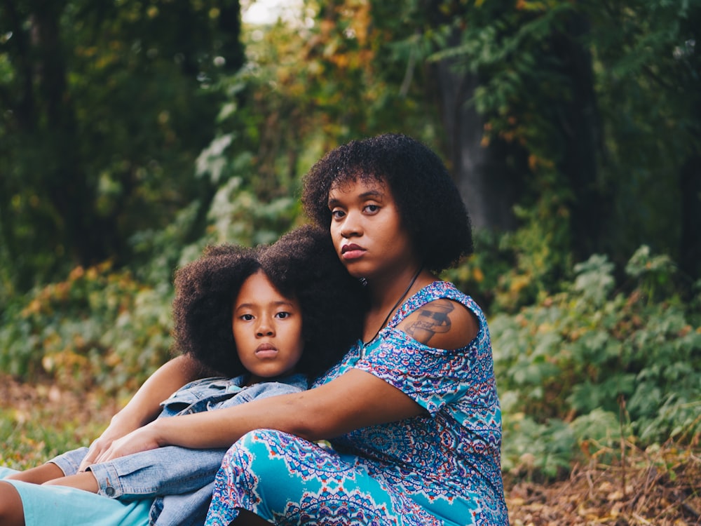 woman sitting in front of child sitting beside trees