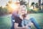 woman holding baby sitting on green grass field under sunset
