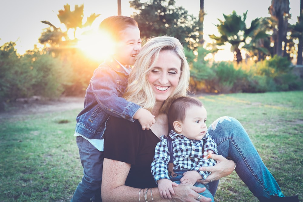 femme tenant un bébé assis sur un champ d’herbe verte sous le coucher du soleil