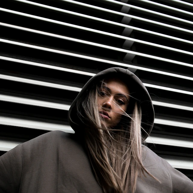 A person in a hoodie standing in front of a plain white wall