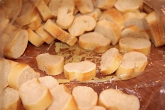 Slices of baguette bread are scattered on a wooden surface, some partially wrapped in clear plastic. The bread slices have a golden crust and a light, airy texture.