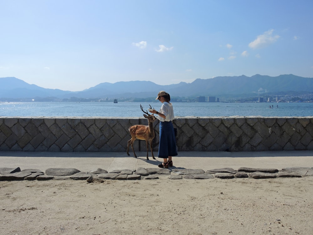 白い長袖シャツを着た女性が、昼間のビーチで茶色のショートコートの犬の横に立つ