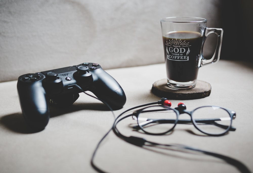 black Sony Dualshock 4 beside clear glass mug filled with coffee
