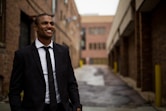 smiling man standing between brown concrete buildings at daytime