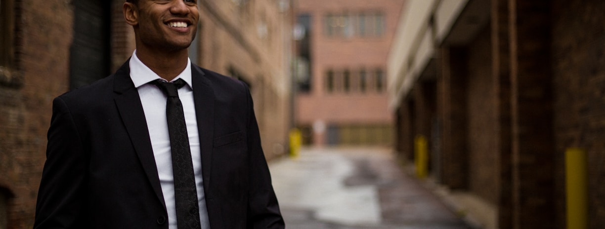 smiling man standing between brown concrete buildings at daytime