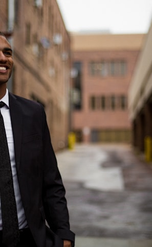 smiling man standing between brown concrete buildings at daytime