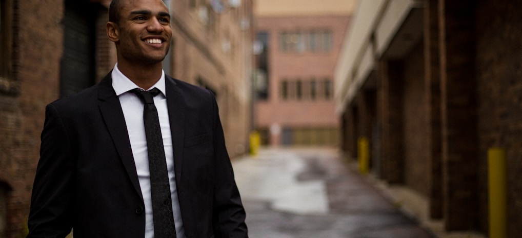 smiling man standing between brown concrete buildings at daytime