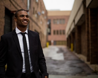 smiling man standing between brown concrete buildings at daytime