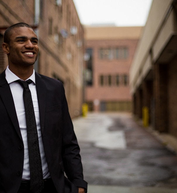 smiling man standing between brown concrete buildings at daytime